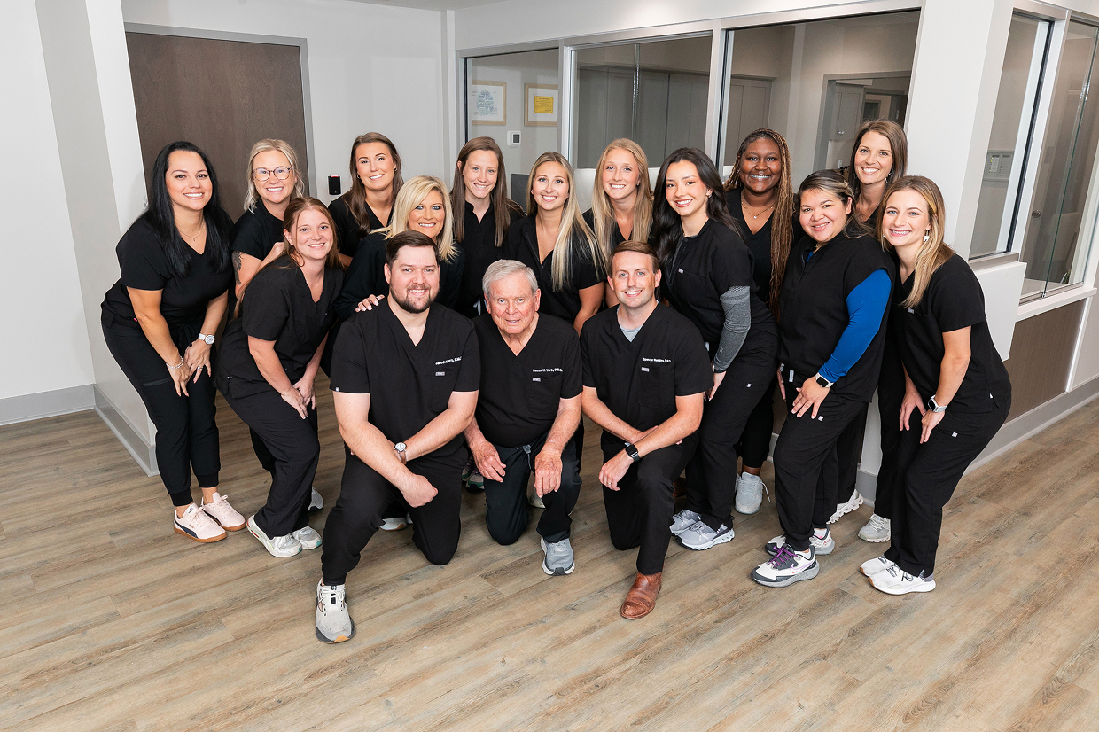 Team of oral surgeons and staff at South Mississippi Oral Surgery & Implant Center in Gulfport, Mississippi, standing together in the clinic lobby wearing black scrubs.